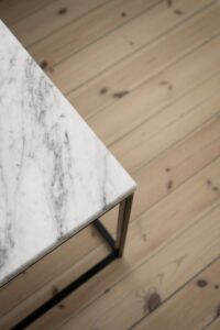 Close-up of a marble table corner with a wooden floor background, highlighting texture and design.