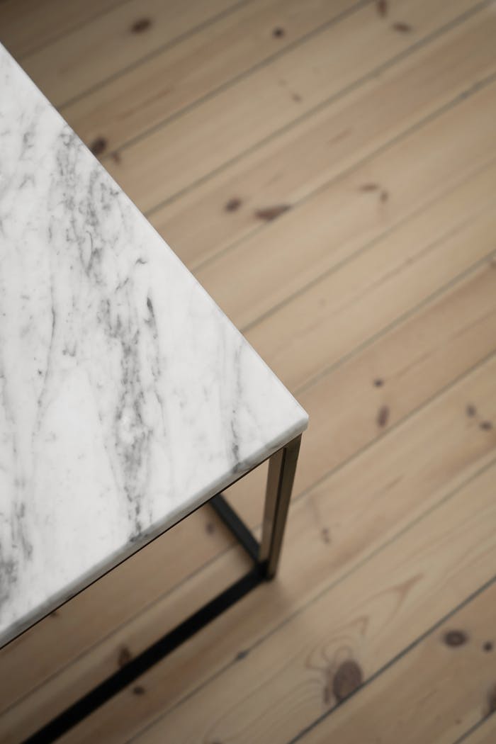 Close-up of a marble table corner with a wooden floor background, highlighting texture and design.