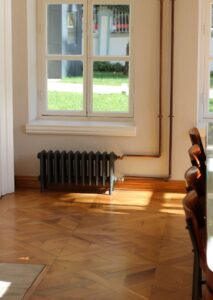 A peaceful sunlit interior featuring a radiator under a window and polished wooden flooring.