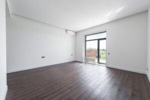 Spacious empty room in new apartment with wooden parquet floor and white wall on sunny day